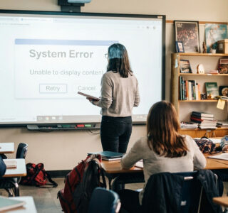 Teacher stands at interactive display that shows error message and students are disengaged